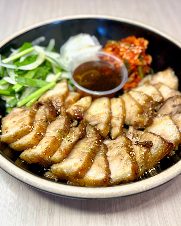 A bowl of bossam with sliced pork belly meat, chopped vegetables and chili sauce from Pocha eats