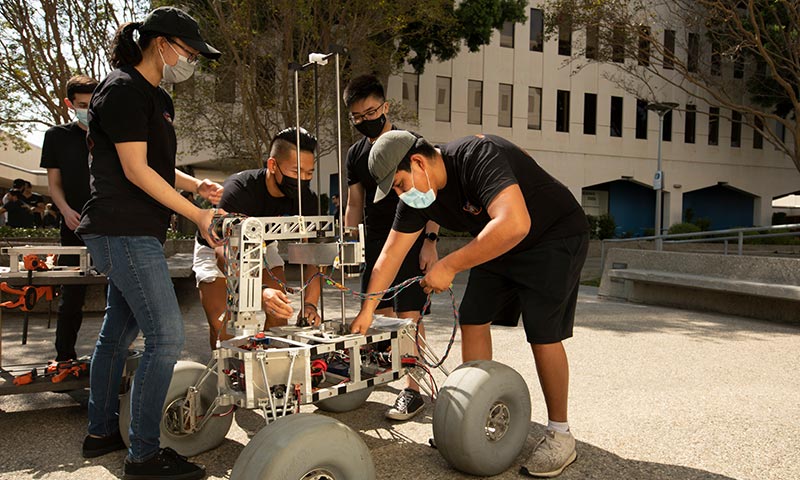 Engineering students and faculty examining a mechanical prototype